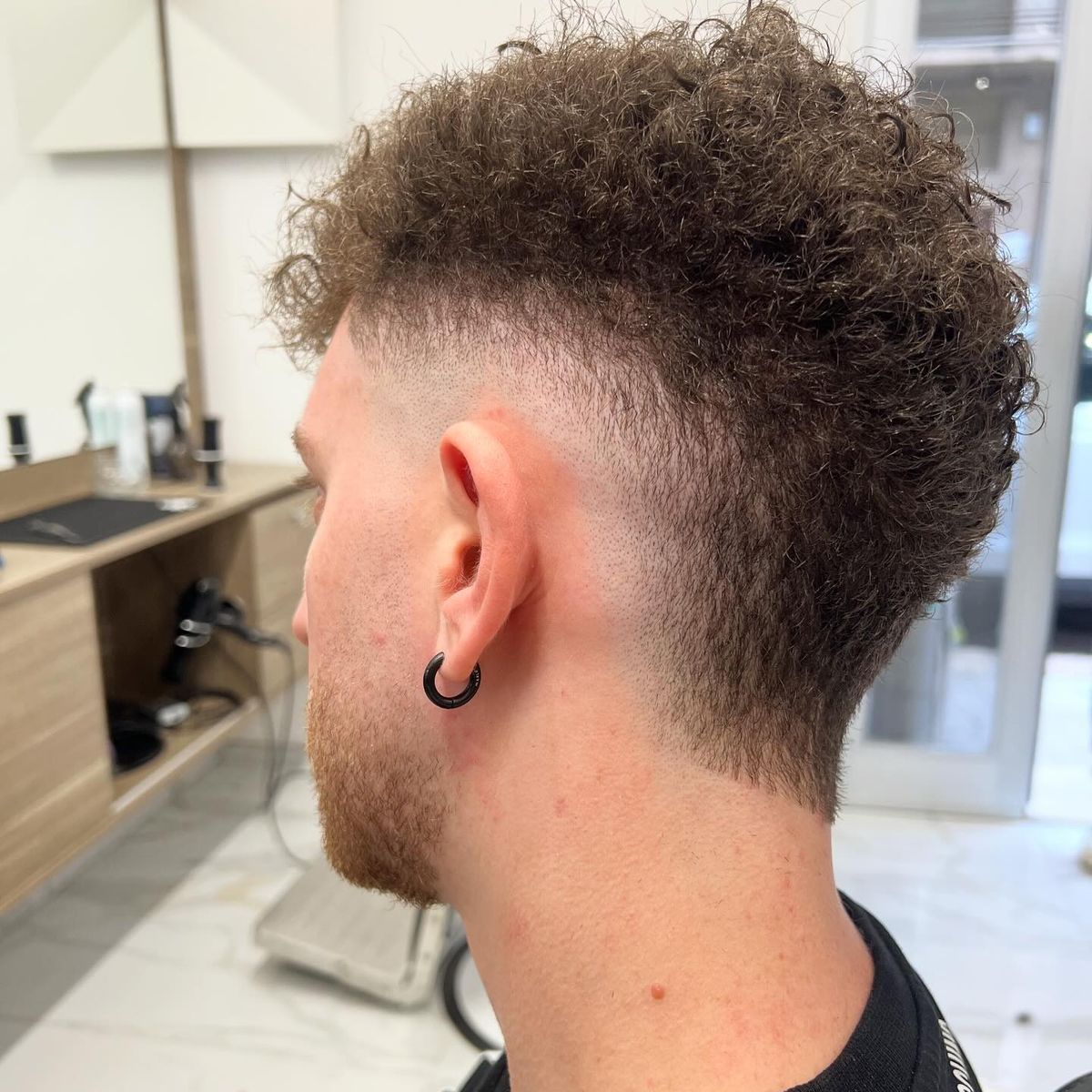 Mullet riccio con burst fade intorno all’orecchio, visto da dietro